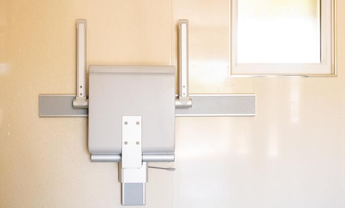 A fold up grey shower chair against a cream wall
